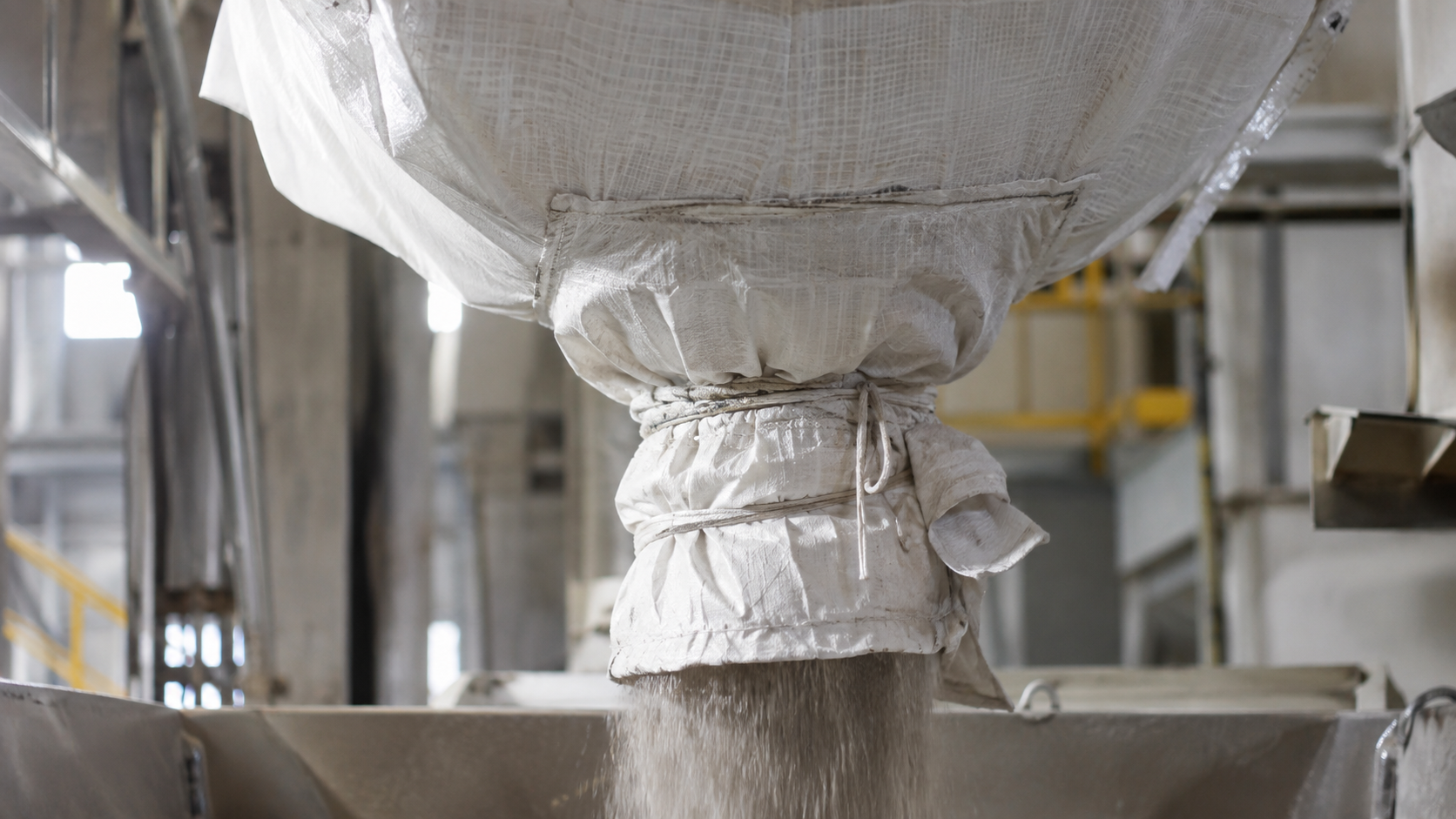 FIBC bottom discharge spout releasing bulk material into industrial receiving equipment